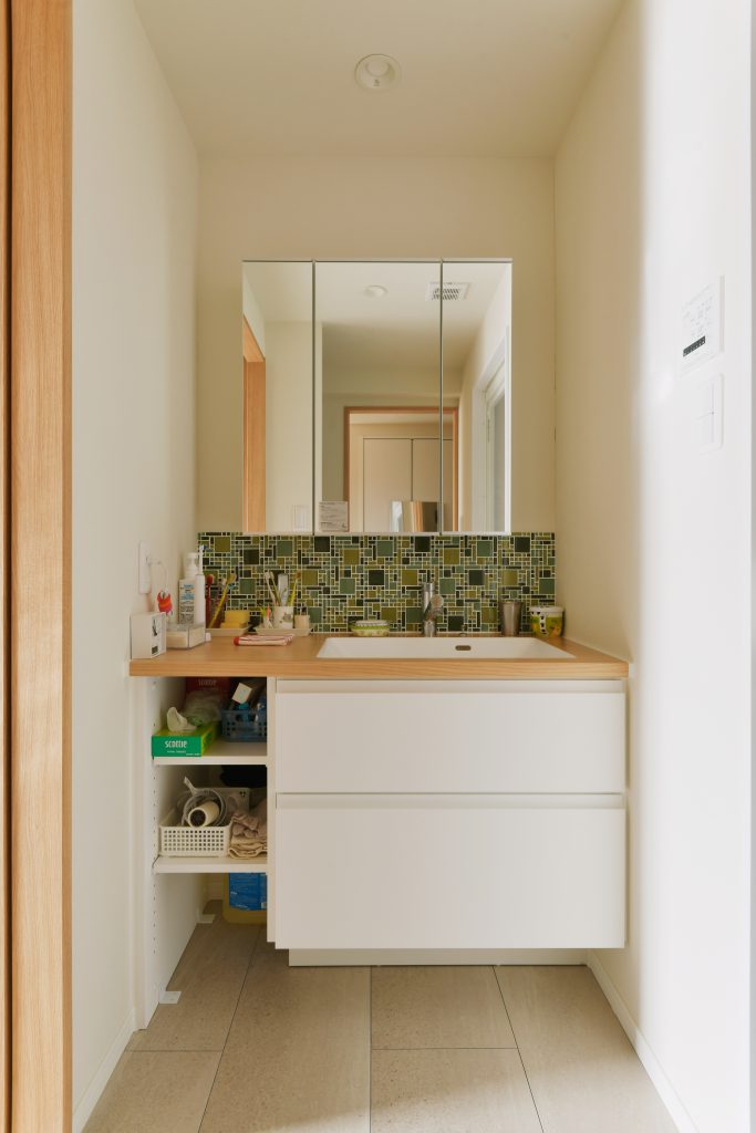 洗面脱衣室：洗面化粧台はアイカのセミオーダー。アクセントタイルには名古屋モザイクのガラスモザイク。解放感だけでなく家事導線も確保しました。廊下、キッチンの両方からアクセスできるようになりました。