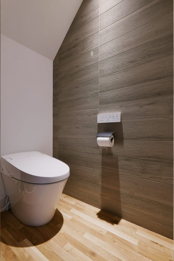 トイレ：木目調のエコカラットを貼り、機能的でありながらもスタイリッシュなトイレになりました。照明にもこだわり、エコカラット面を照らすように設置しています。